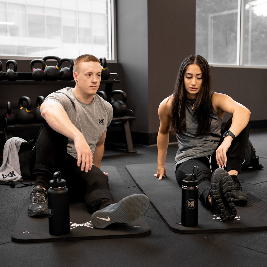 IXK Gear Quick Dry Tank in Colour: Charcoal. Gym background. Male model is wearing IXK Gear Cotton Tee in Colour: Grey with Slim Sweats Trackies n colour: Black. Pictued at the front is the IXK Gear Hot and Cold Bottle in 1l and 500ml.