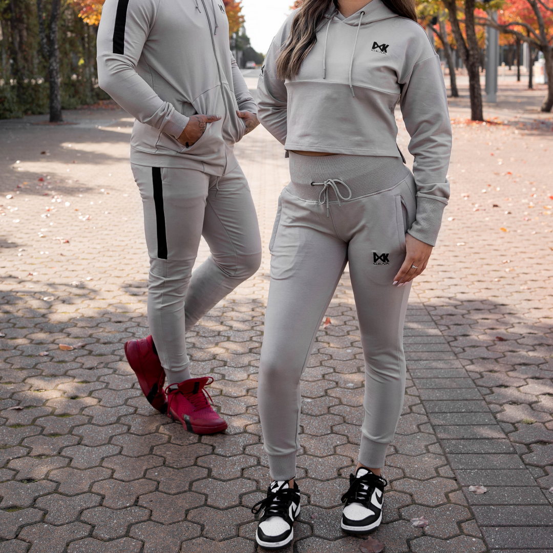 IXK Gear Women's Tracksuit in colour: Stone. Two-Piece tracksuit which includes slightly cropped hoodie and slim-fit trackpants trackies with zip pockets. Natural background. Male model is wearing the IXK Gear Men's Tracksuit in Stone.