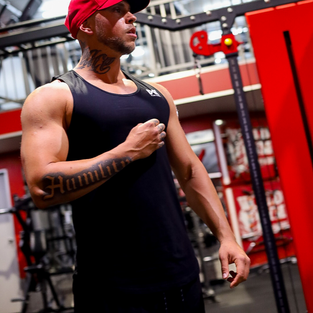 Male model wearing Muscle Tank Top in Black. Gym background.